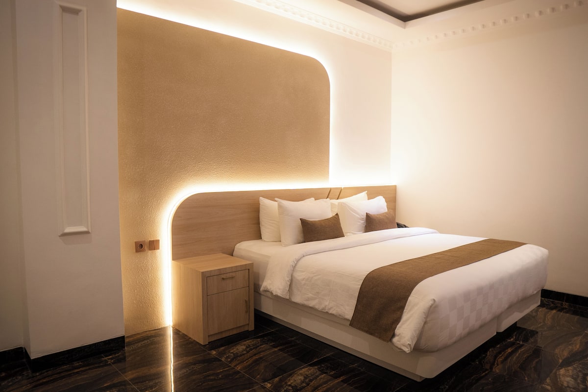 Una habitación de hotel moderna con una cama grande, una mesita de noche y un cabecero empotrado con iluminación integrada.