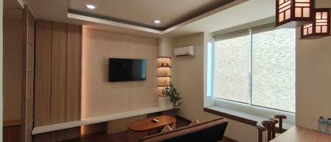 Una sala de estar moderna con un televisor de pantalla plana, un sofá, una mesa de comedor y un ventanal grande.