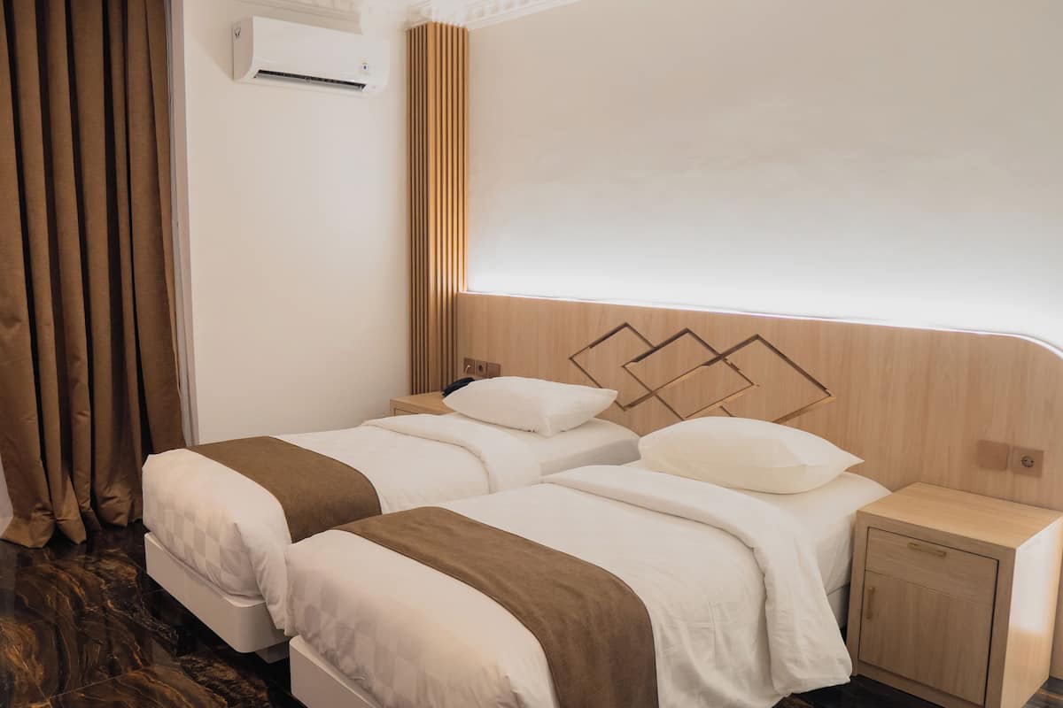 Habitación de hotel con dos camas, una mesita de noche, un cabecero de madera y un aire acondicionado de pared.