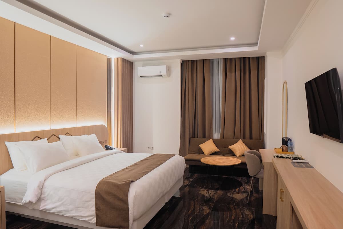 Una habitación de hotel con cama, sofá, escritorio, televisor y aire acondicionado.