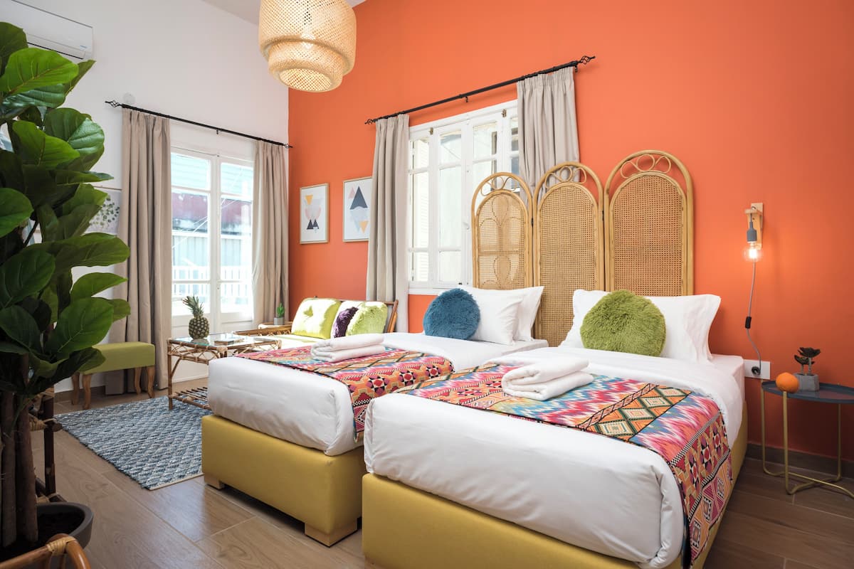 Ein Hotelzimmer mit zwei Betten, einem großen Fenster, einem Rattan-Kopfende und einem Blumentopf.