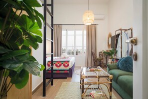 Una sala de estar acogedora con una cama, un sofá verde, una mesa de centro y una lámpara colgante.