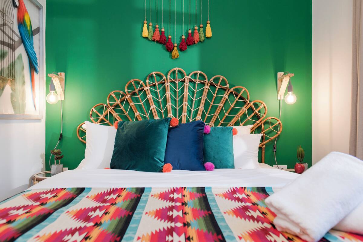 Ein Bett mit einem farbenfrohen, gemusterten Überwurf, einer grünen Wand und einem dekorativen Kopfteil mit hängenden Quasten.