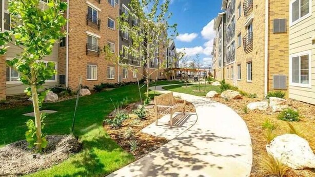 A multi-story residential building with a landscaped courtyard, a pathway, and outdoor seating.
