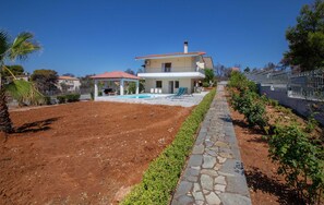 Una casa de dos pisos con piscina, un patio cubierto y un camino de piedra.