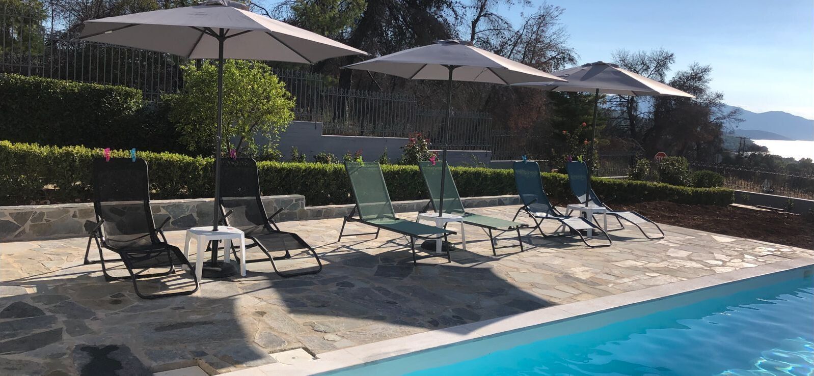 A poolside area with lounge chairs and umbrellas, a stone patio, and a view of the sea.