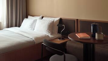 A hotel room with a bed, a desk with a lamp, a coffee maker, and a chair.