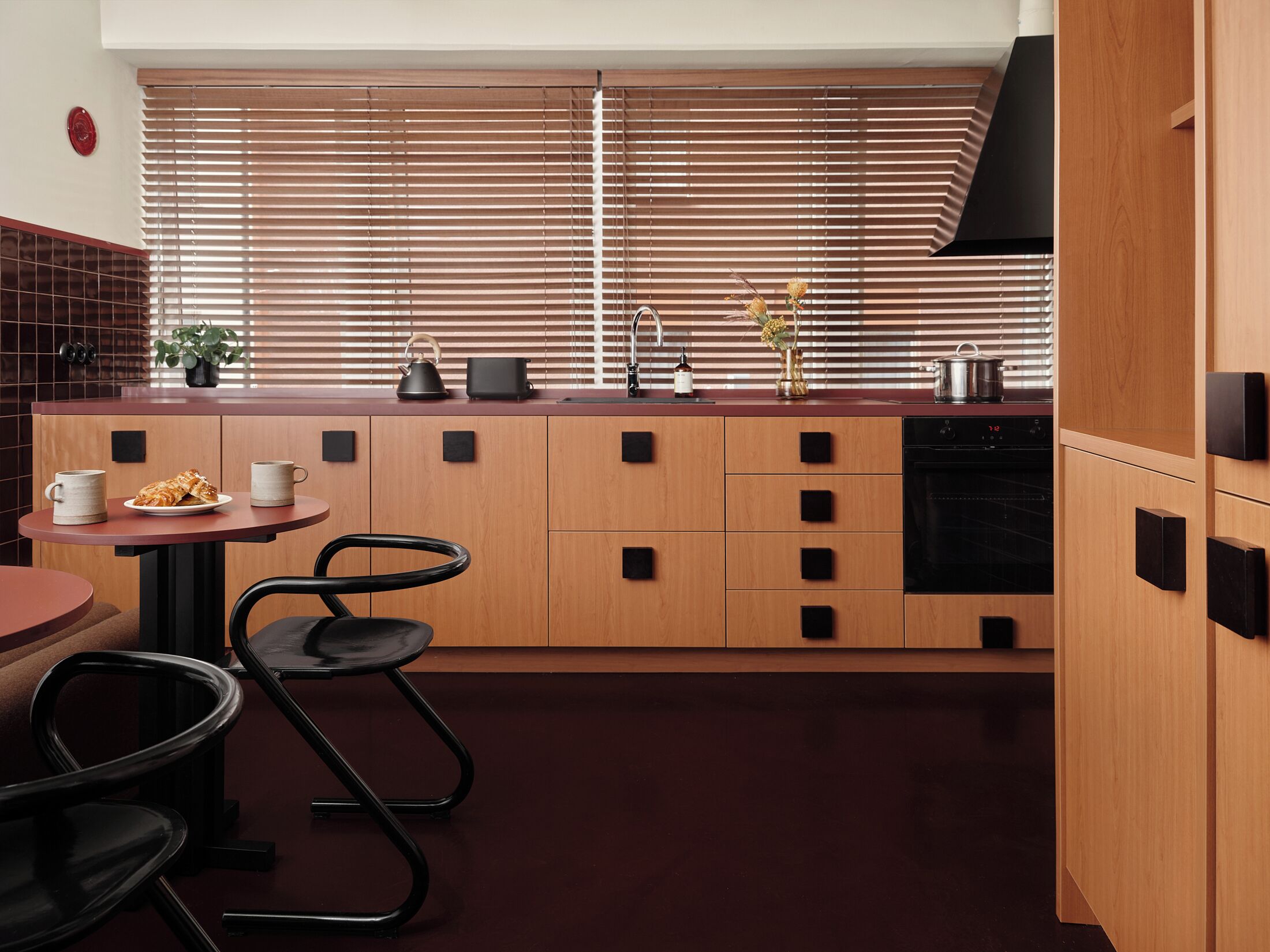 A modern kitchen with wooden cabinets, a black stove, and a dining area with a table and chairs.