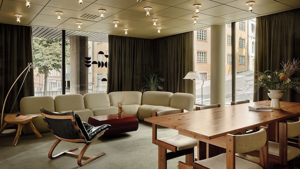 A modern hotel room with a large window, a sofa, a wooden dining table, and a lamp. - Bob W Stockholm Norrmalm (Stockholm)