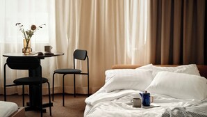 A hotel room with a bed, a small table with a vase of flowers, a chair, and a coffee pot on the bed. - Bob W Stockholm Norrmalm (Stockholm)