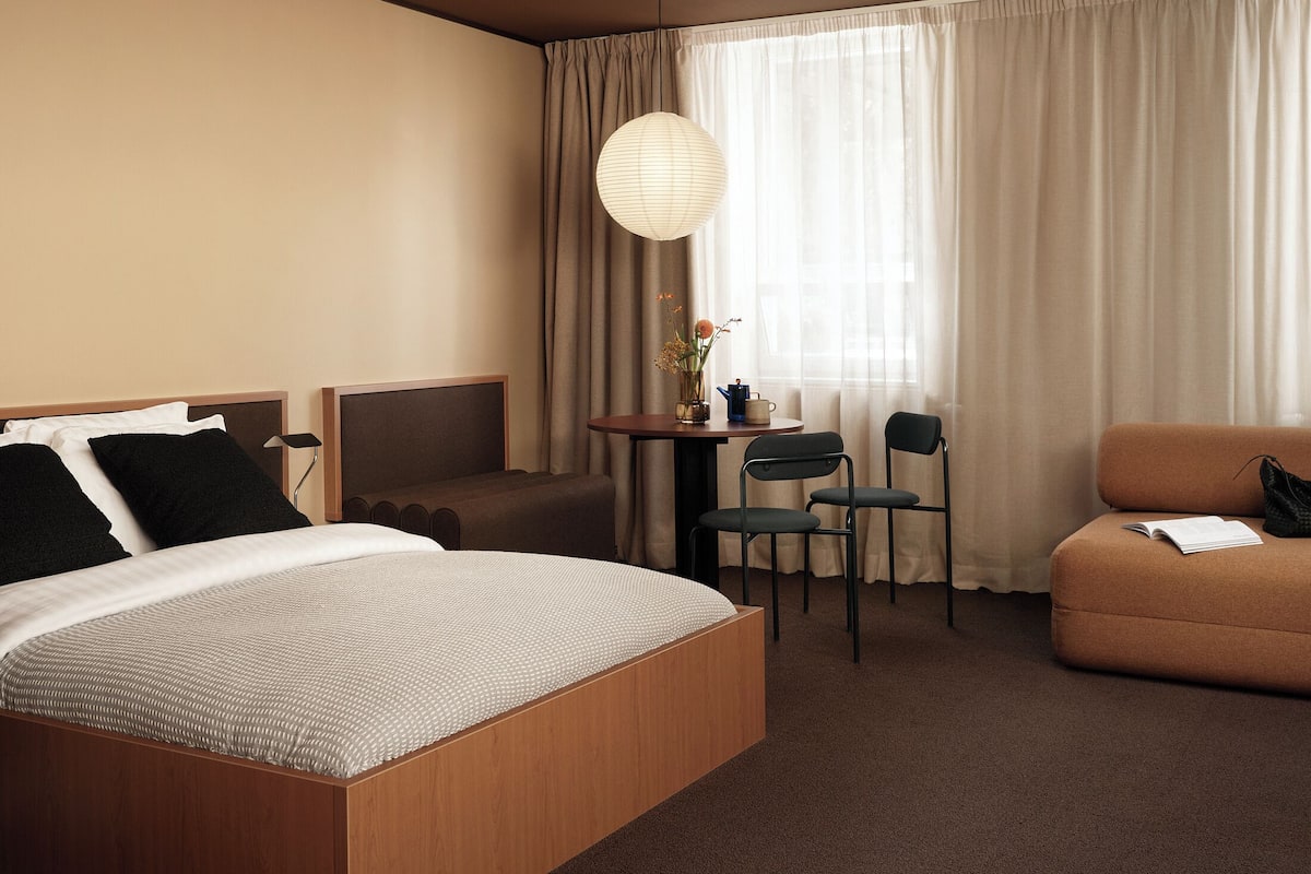 A hotel room with a large bed, a sofa, a small table with chairs, and a hanging light fixture.