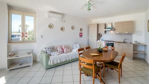 A modern kitchen with a dining area, a sofa, and a small shelf with decorative items. - Casa Sogno Salentino Garden Ac (Porto Cesareo)