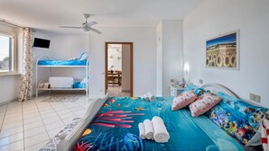 A bedroom with a bunk bed, a ceiling fan, a bed with a blue ocean-themed bedspread, and a painting of sunflowers on the wall. - Casa Sogno Salentino Garden Ac (Porto Cesareo)