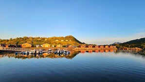 A waterfront property with a row of cabins, a dock with boats, and a hill with houses in the background. - Fjordcamp AS (Straumsjøen)