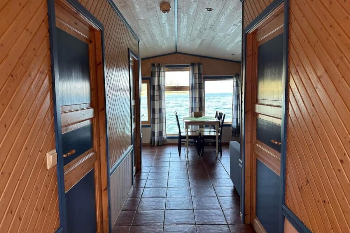 A corridor with wooden walls and a tiled floor leading to a dining area with a table and chairs.