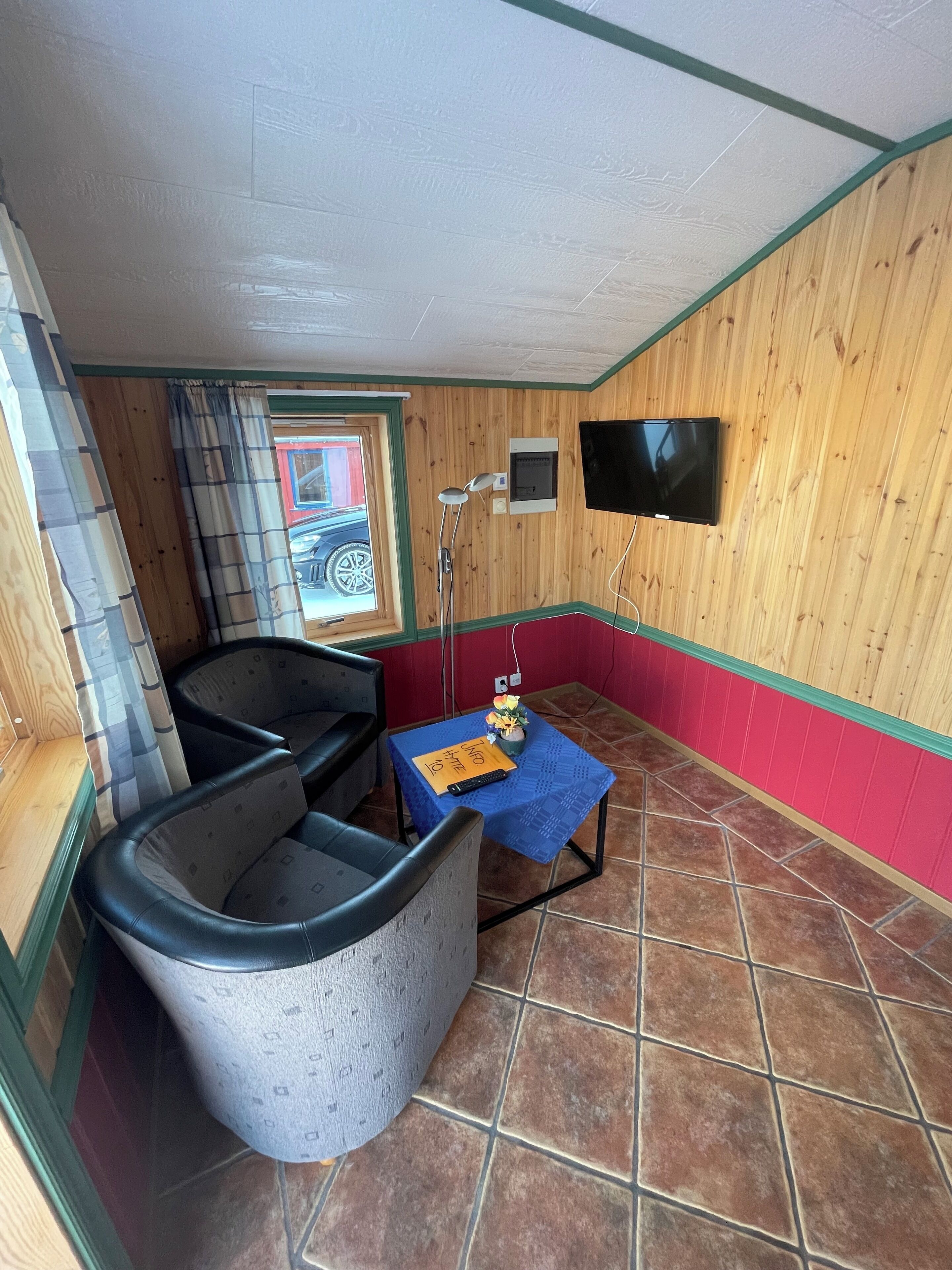 Une pièce avec un plancher en bois, une table bleue avec une télécommande, un téléviseur et une fenêtre avec des rideaux.