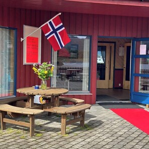 A wooden picnic table with a vase of flowers, a flag, and a sign on the building's exterior.