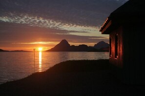 A sunset over a calm body of water with a silhouette of a mountain and a building with vertical lines.
