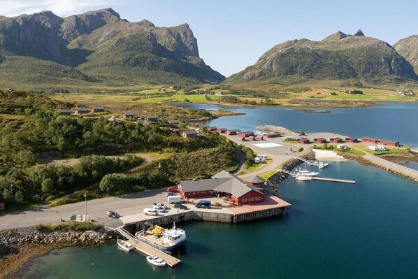 A coastal marina with boats docked, a red building, and a mountainous backdrop.