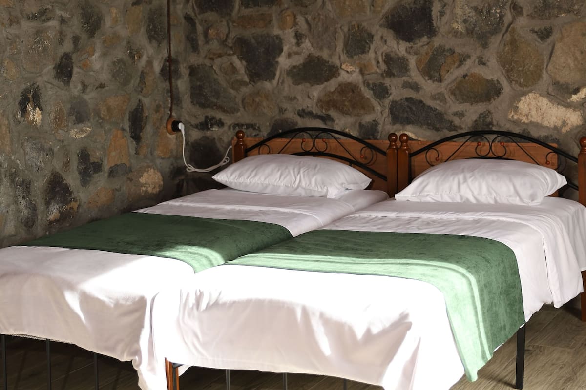 A room with a stone wall, a wooden ceiling, and a bed with a green bedspread.