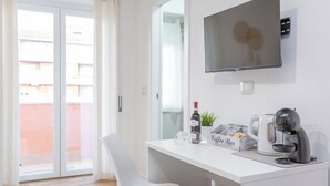 Una habitación moderna con un escritorio blanco, una silla, una cafetera y un televisor montado en la pared.