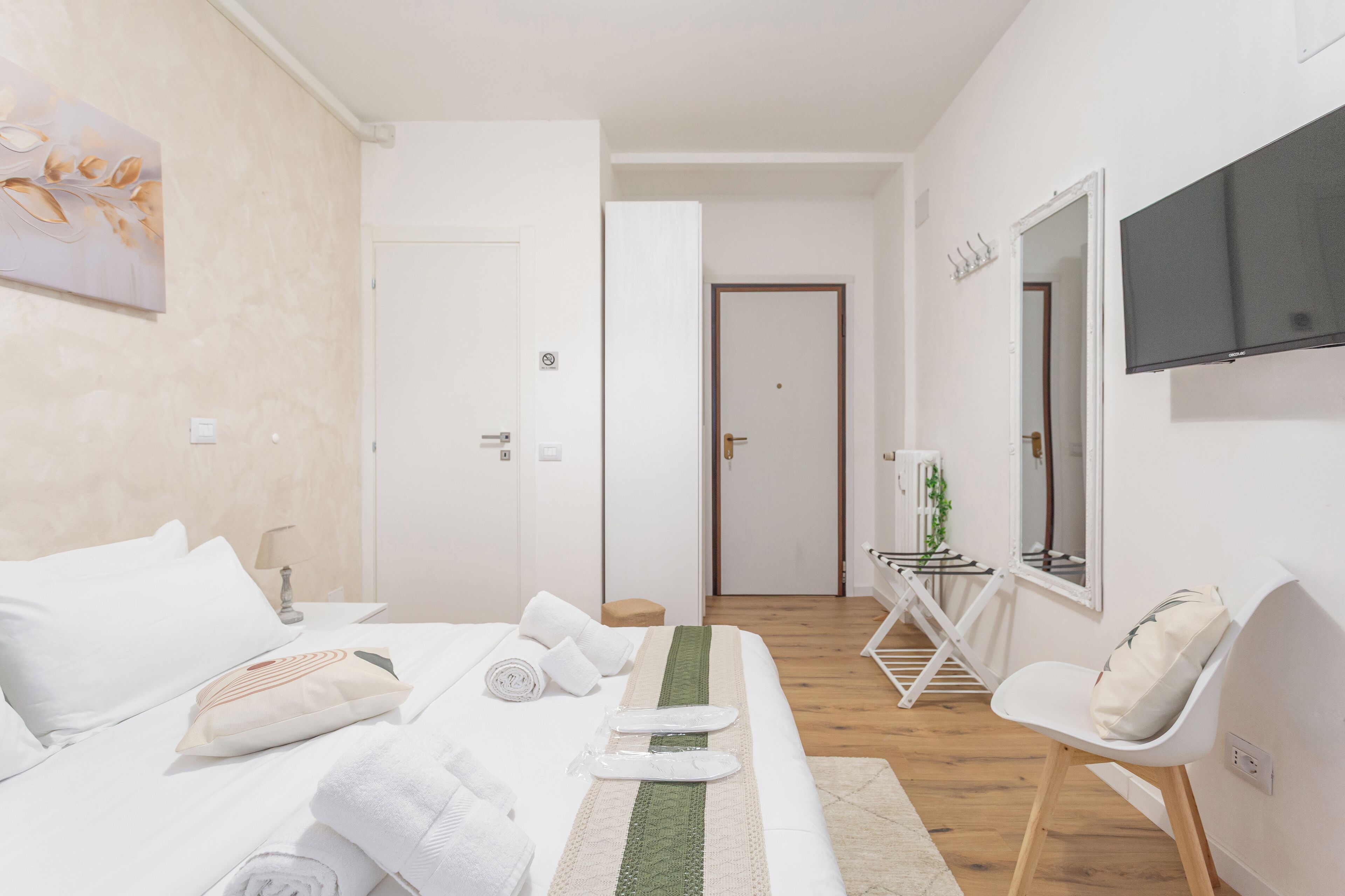 Ein modernes Hotelzimmer mit einem ordentlich bezogenen Bett, einer Sitzecke mit Sessel und kleinem Tisch, einem an der Wand montierten Flachbildfernseher und einer Tür zu einem weiteren Raum.