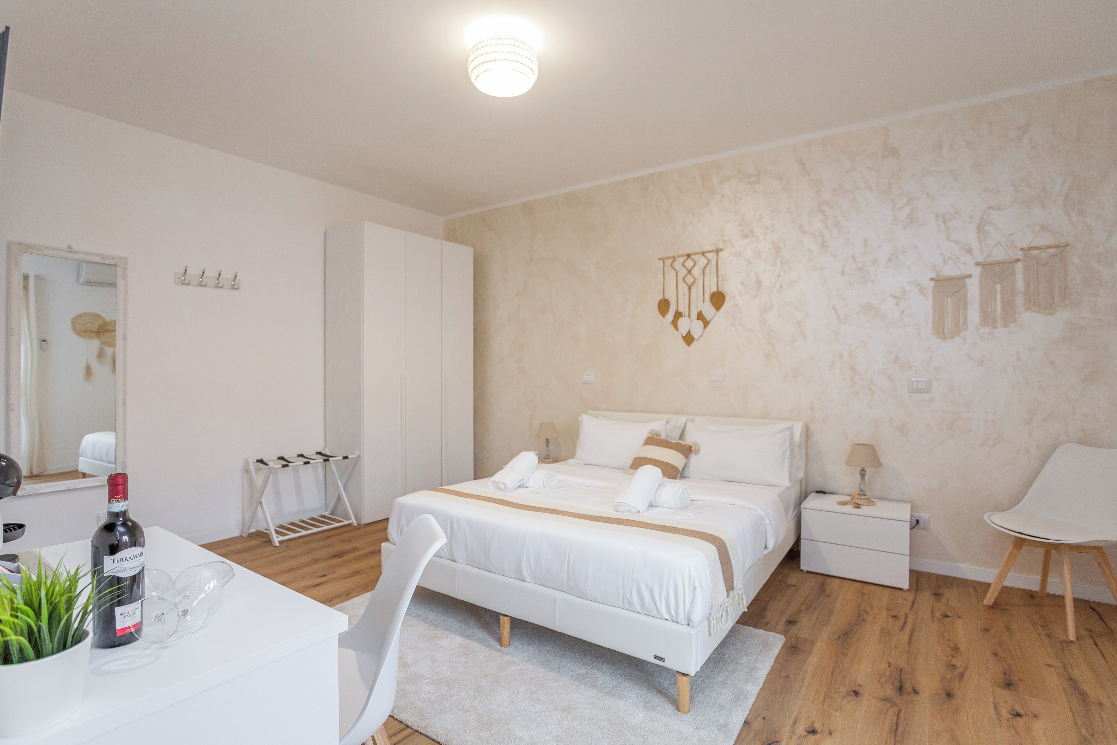 A modern bedroom with a bed, bedside table, chair, and a small desk with a plant and a bottle.