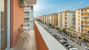 A balcony with a table and chairs, overlooking a street with parked cars and multi-story buildings. - Pampas Roma (Rome)
