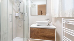 A modern bathroom with a glass-enclosed shower, a white sink, and a wooden vanity. - Pampas Roma (Rome)