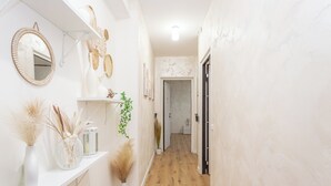 A hallway with a wooden floor, white walls, and a white shelf with decorative items. - Pampas Roma (Rome)