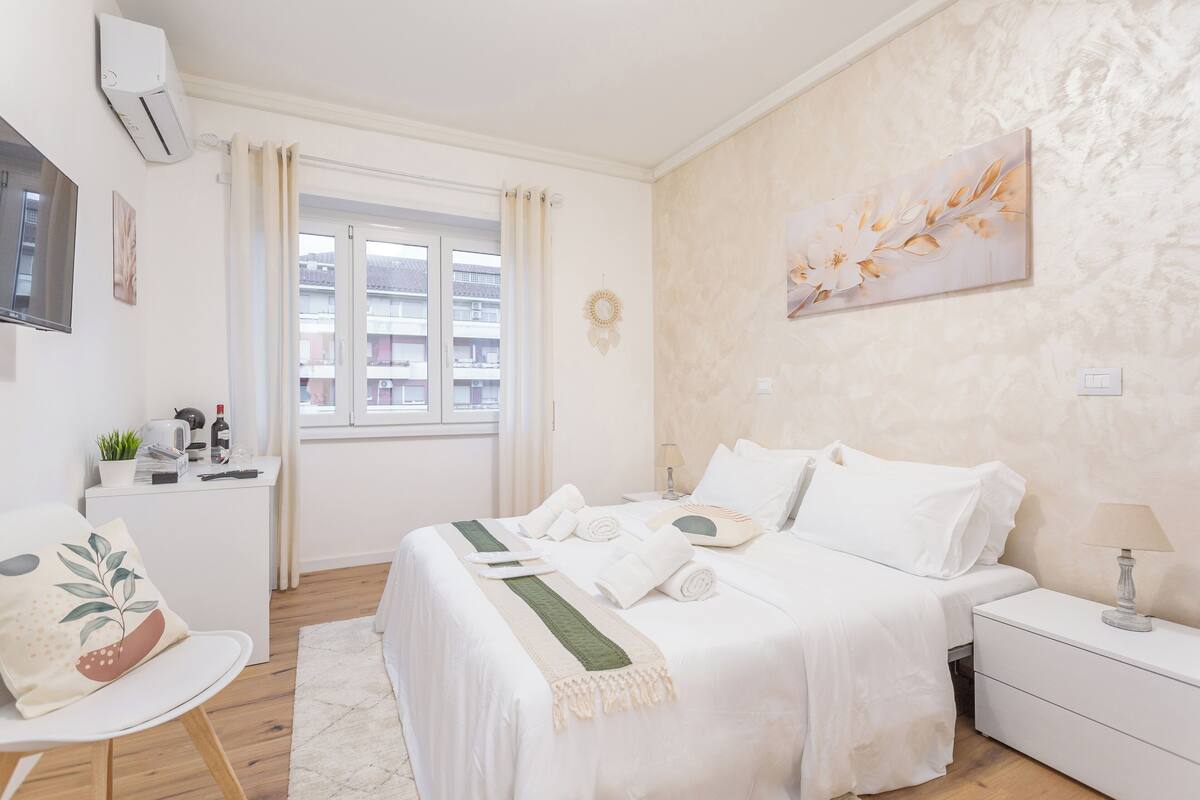 A hotel room with a bed, bedside table, chair, and a window with curtains.