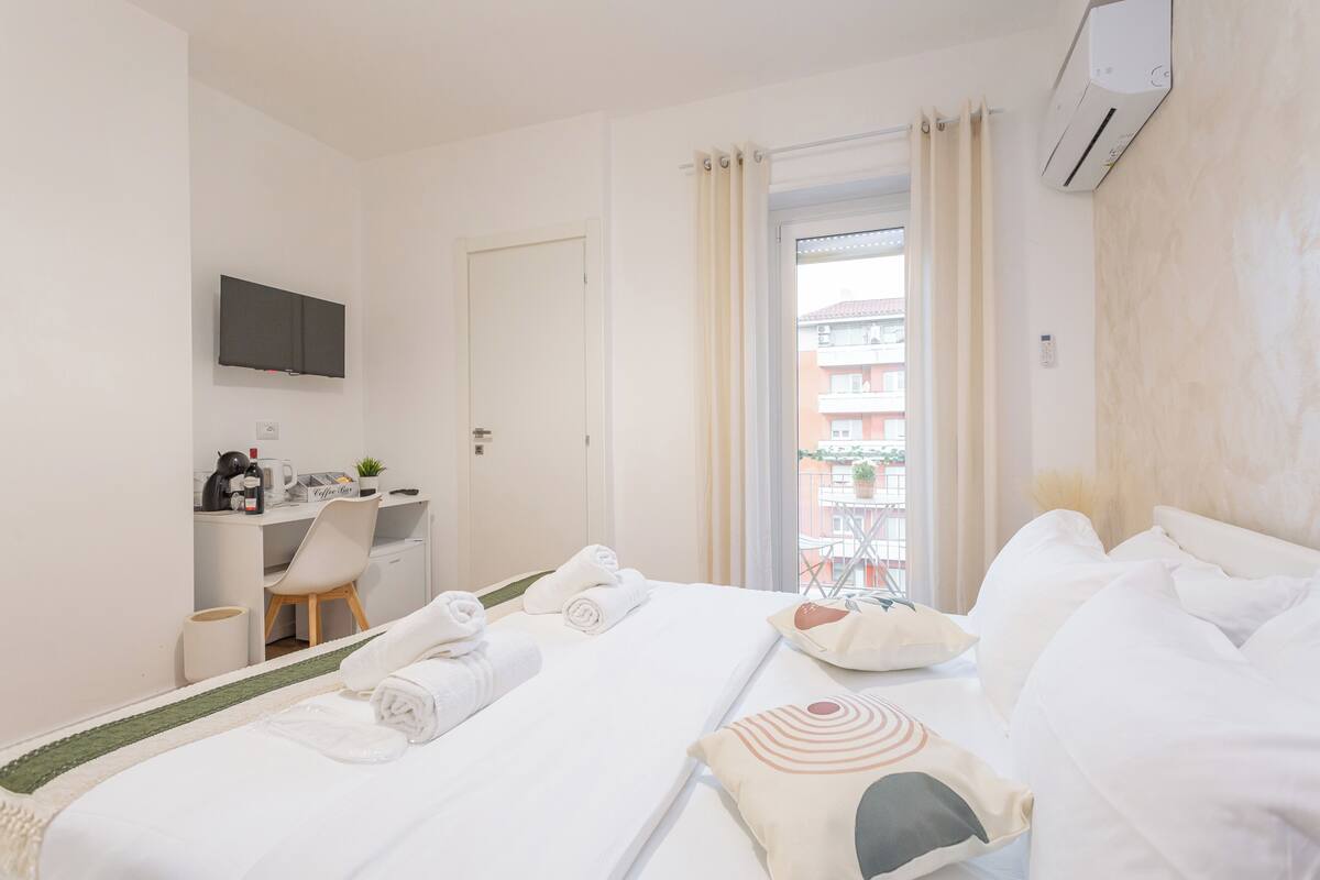 A hotel room with a bed, a desk with a chair, a television, and a window with curtains.