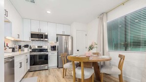 A modern kitchen with white cabinets, stainless steel appliances, a dining table with chairs, and a window with blinds. - Cheery Lynn I Cozy Luxe Escape (Scottsdale)