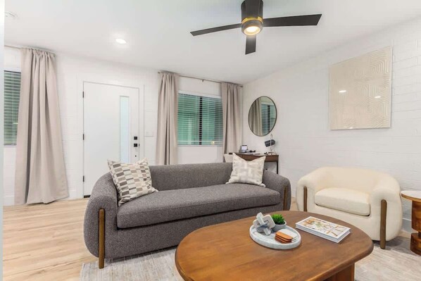 A modern living room with a grey sofa, a white armchair, a wooden coffee table, and a ceiling fan. - Cheery Lynn II Soft & Stylish Stay (Scottsdale)