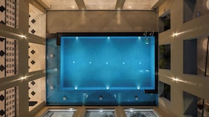 Una amplia piscina interior con agua azul cristalina, rodeada de paredes con diseños geométricos y un estilo moderno.