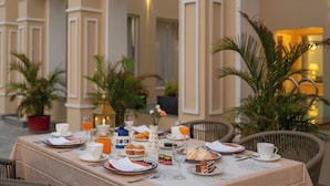 Un área de comedor al aire libre con una mesa dispuesta para el desayuno, incluyendo platos, tazas y diversas opciones de comida.