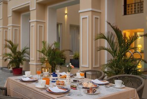 An outdoor dining area with a table set for breakfast, including plates, cups, and a variety of food items.