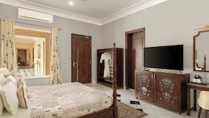 Un dormitorio con cama, armario, televisor y baño visible a través de una puerta abierta.