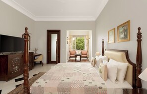 A bedroom with a large bed, a television, a desk, and a chair. There is a window with a view of trees. - Chez Lavania A Boutique stay (Udaipur)