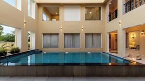 A modern indoor swimming pool with a clear view of the surrounding architecture, including a balcony with decorative railings and a staircase. - Chez Lavania A Boutique stay (Udaipur)