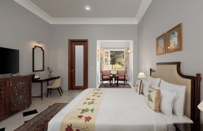 A hotel room with a bed, a desk, a television, a mirror, and a door leading to a balcony. - Chez Lavania A Boutique stay (Udaipur)