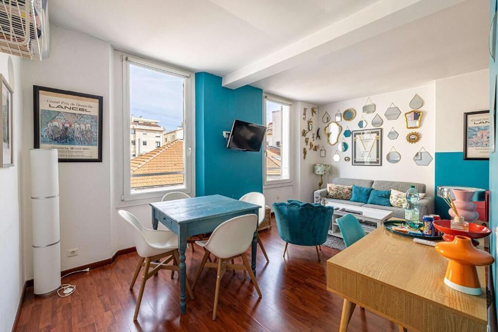 Ein modernes Wohnzimmer mit blauer Akzentwand, einem Essbereich mit Holztisch und -stühlen sowie einer Sofagarnitur.