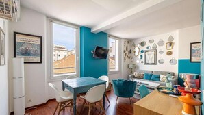 A modern living room with a blue accent wall, a dining area with a wooden table and chairs, and a sofa set. - Le Miroir d'André séjour bonheur au cœur de Cannes (Cannes)