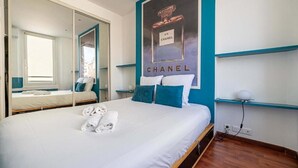 A hotel room with a large bed, a mirror, a Chanel poster, and a window. - Le Miroir d'André séjour bonheur au cœur de Cannes (Cannes)