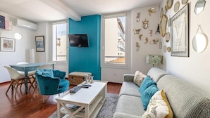 A modern living room with a teal accent wall, a flat-screen TV, a dining area with chairs, and a sofa with decorative pillows. - Le Miroir d'André séjour bonheur au cœur de Cannes (Cannes)