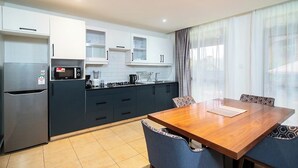 Eine moderne Küche mit integriertem Mikrowellenherd, Herd und Kühlschrank. Ein Esstisch mit Stühlen und ein Fenster mit Vorhängen sind ebenfalls vorhanden.