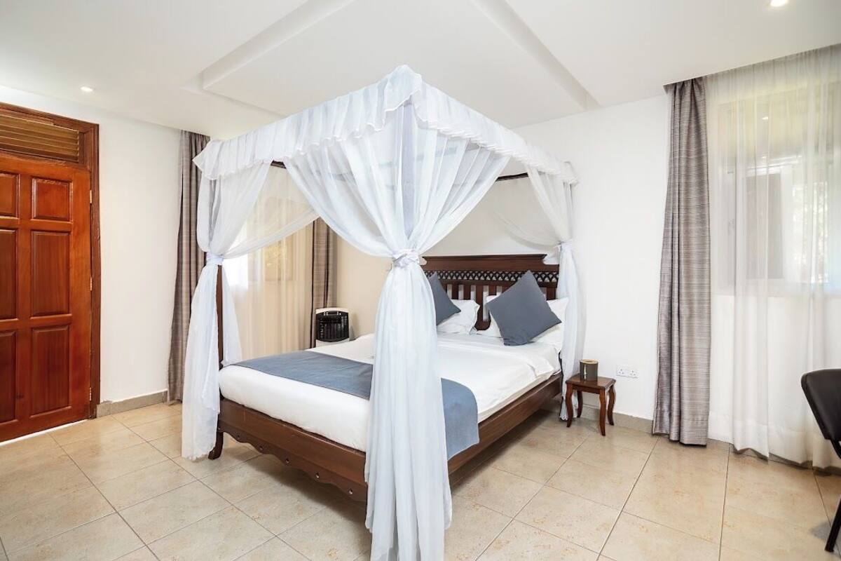 A bedroom with a four-poster bed, a wooden headboard, a bedside table with a lamp, and a chair.