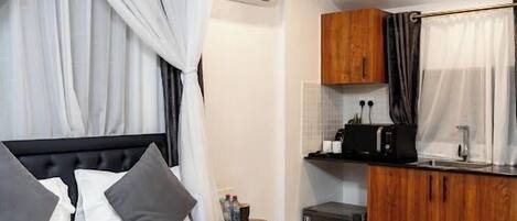 Un dormitorio moderno con una cama grande, una kitchenette pequeña y un baño.