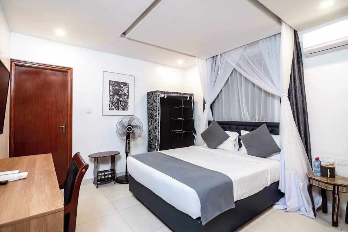 A bedroom with a bed, bedside table, and a standing fan.