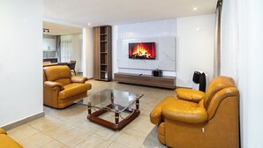 Ein Wohnzimmer mit zwei Ledersofas, einem Glastisch, einem an der Wand befestigten Fernseher und einem Kamin.